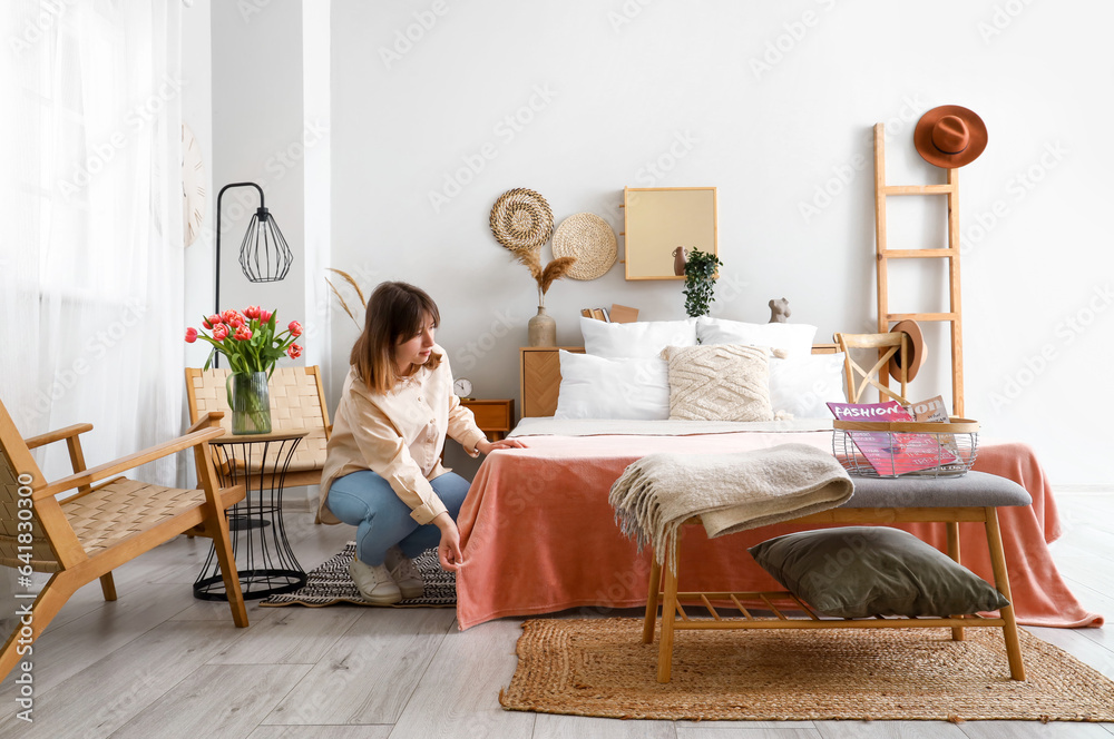 Young woman making bed in light bedroom