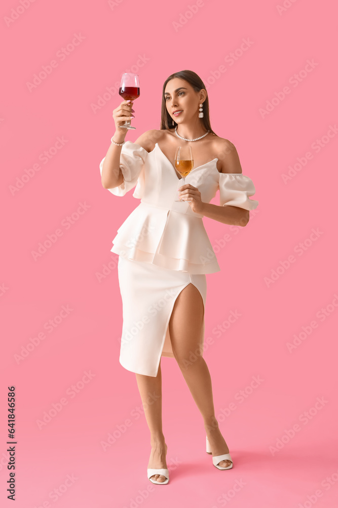 Young woman with glasses of wine on pink background