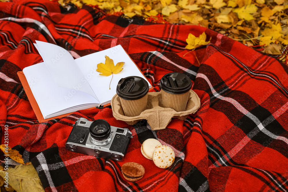 Book with autumn leaf, cups of coffee, macaroons and photo camera on plaid in park