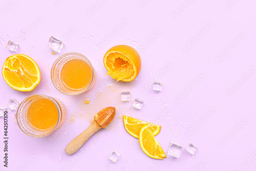 Glasses of orange juice with ice cubes and juicer on lilac background