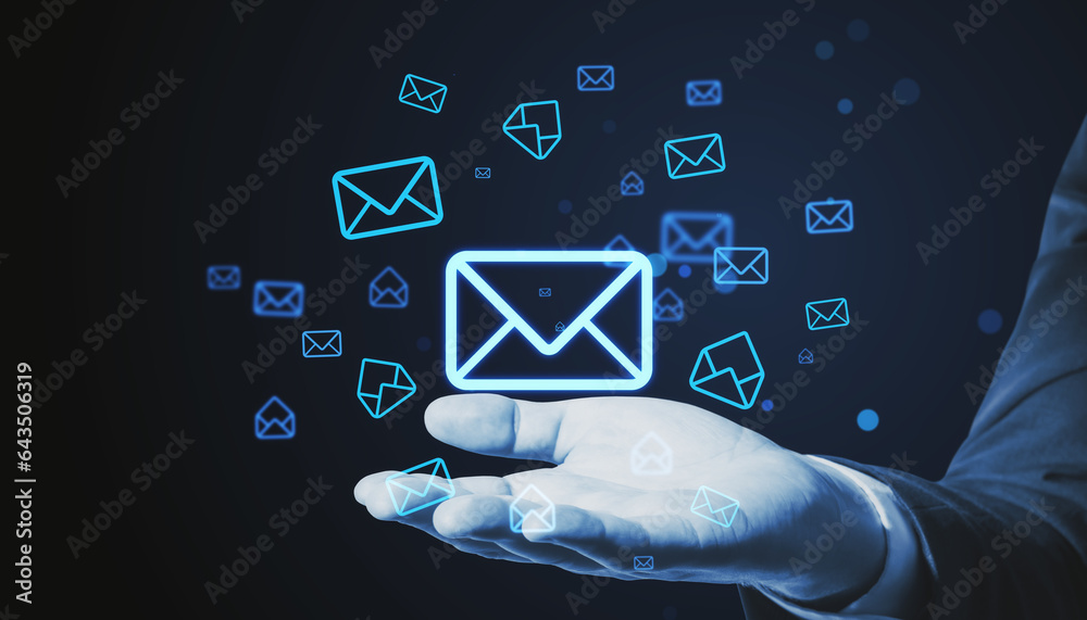 Close up of businessman hand holding glowing email letter icons on dark blue background. Communicati