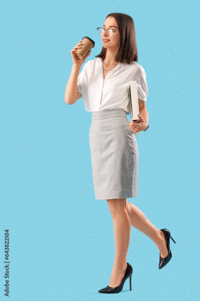 Young businesswoman with folder and cup of coffee on blue background