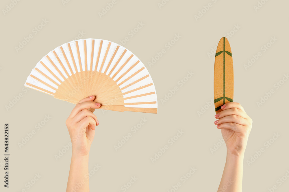 Female hands with mini surfboard and fan on grey background