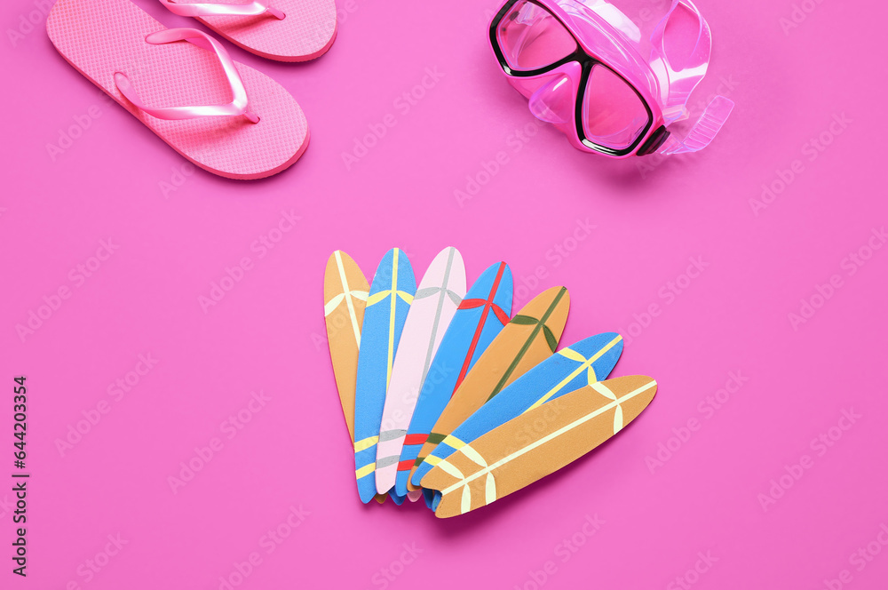 Different mini surfboards, snorkeling mask and flip-flops on pink background