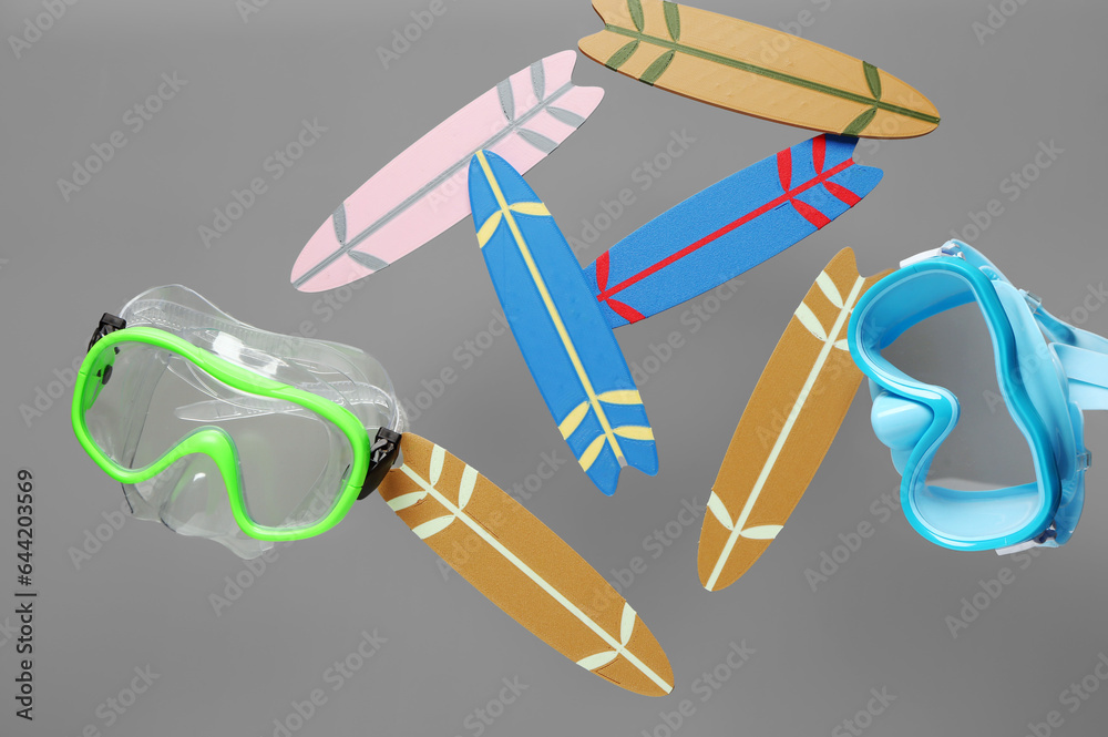 Flying mini surfboards and snorkeling masks on grey background