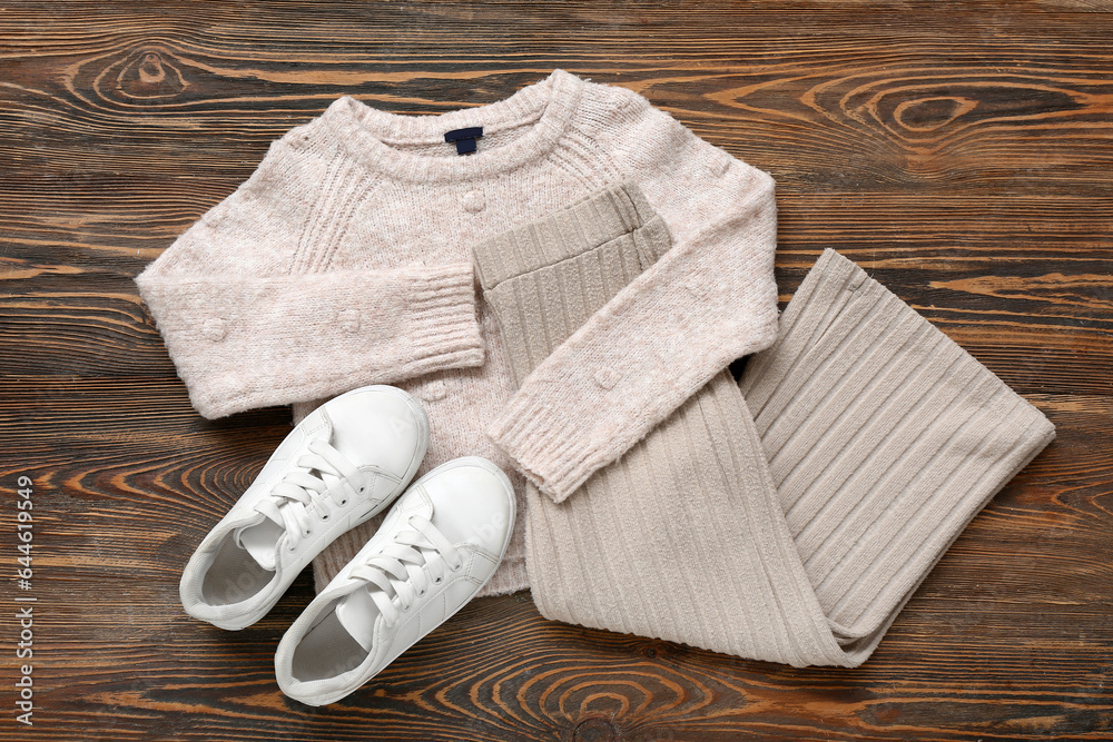 Stylish childrens sweater, pants and shoes on wooden background