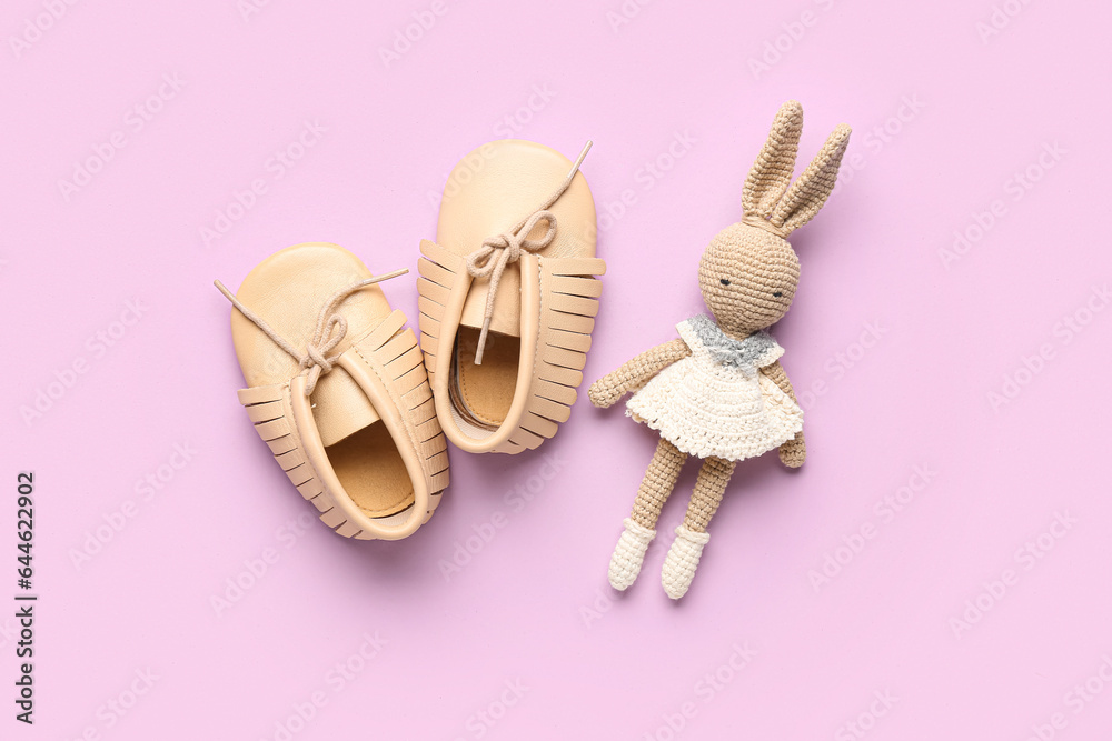 Stylish baby booties and knitted toy on pink background