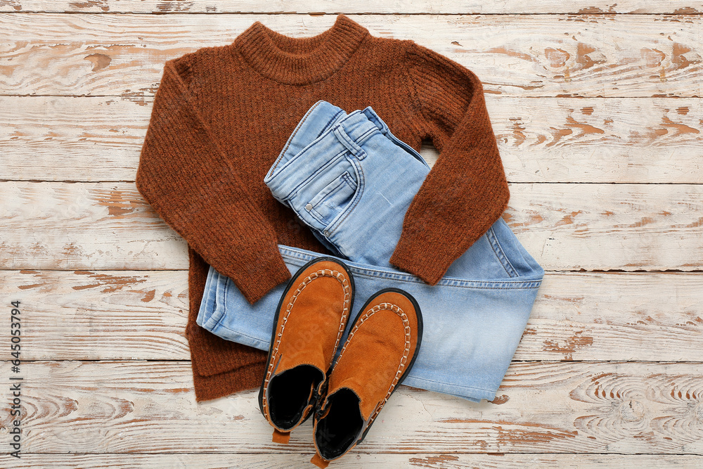 Stylish childrens sweater, jeans and boots on light wooden background