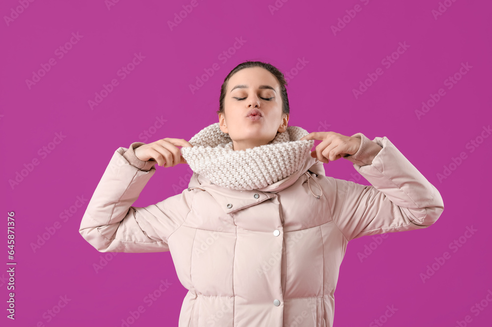 Young woman in down coat blowing kiss on purple background