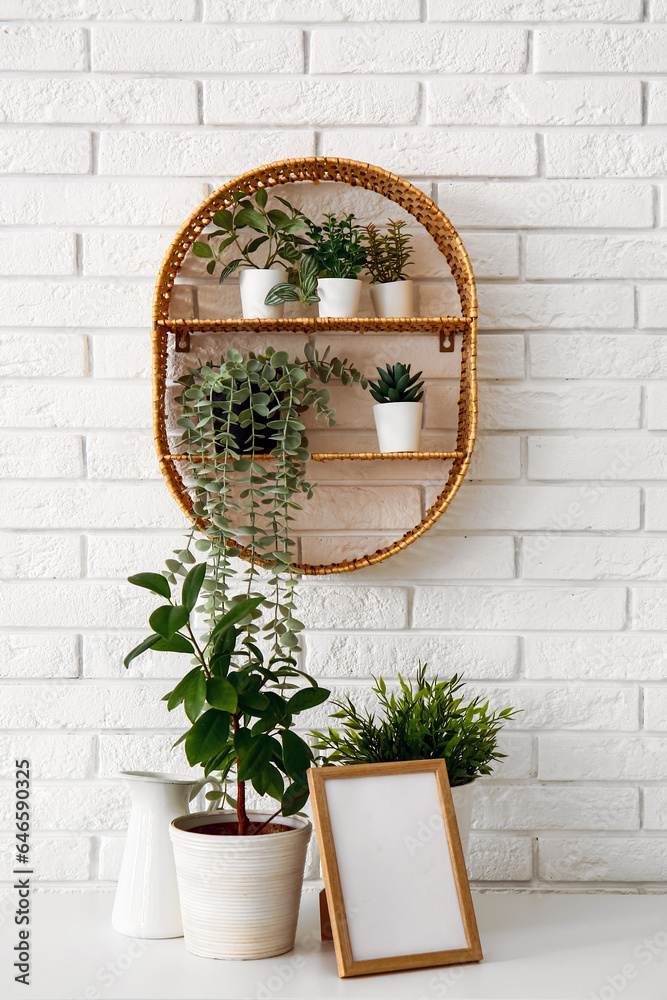 Green houseplants with frame on shelf near white brick wall