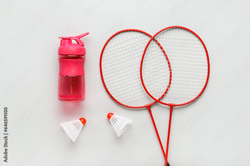 Badminton  rackets, shuttlecocks and bottle of water on light background