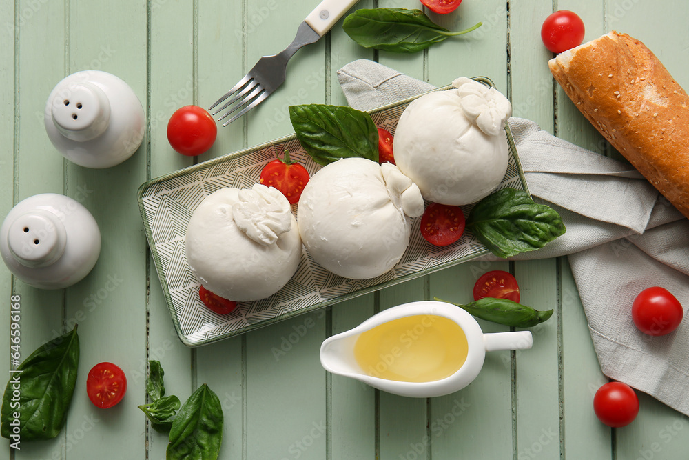 Plate of tasty Burrata cheese with basil and tomatoes on green wooden background