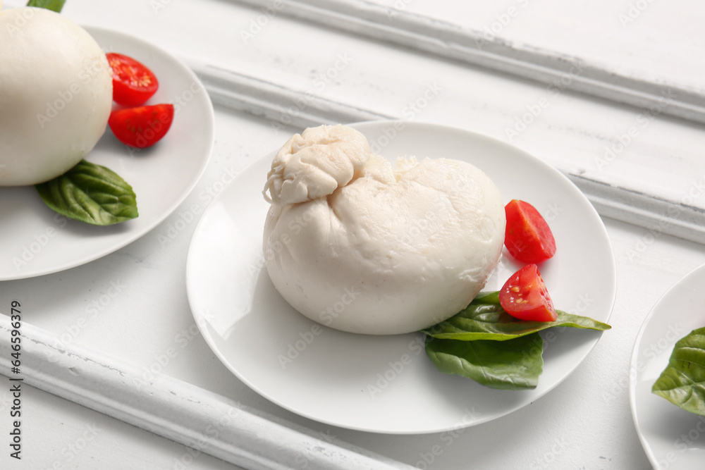 Plates of tasty Burrata cheese with basil and tomatoes on white background
