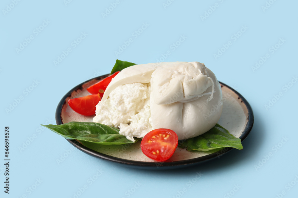 Plate of tasty Burrata cheese with basil and tomatoes on blue background