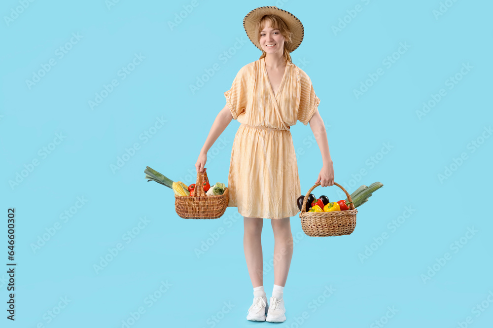 Young female farmer with wicker baskets full of different ripe vegetables on blue background