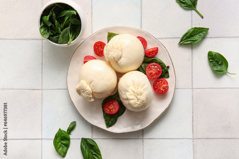 Plate of tasty Burrata cheese with basil and tomatoes on white tile background