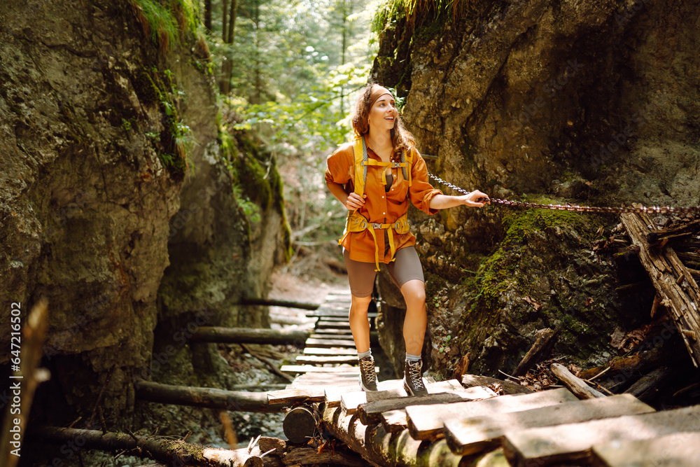 Happy woman in hiking clothes with a yellow backpack walks along a wooden hiking path in the mountai