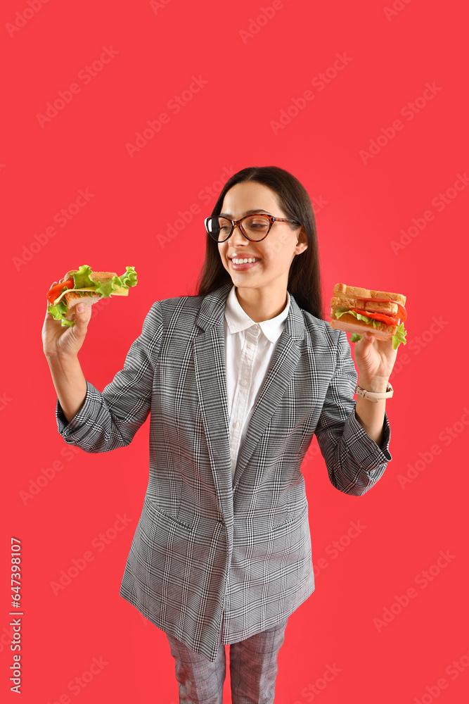 Young businesswoman with tasty sandwiches on red background