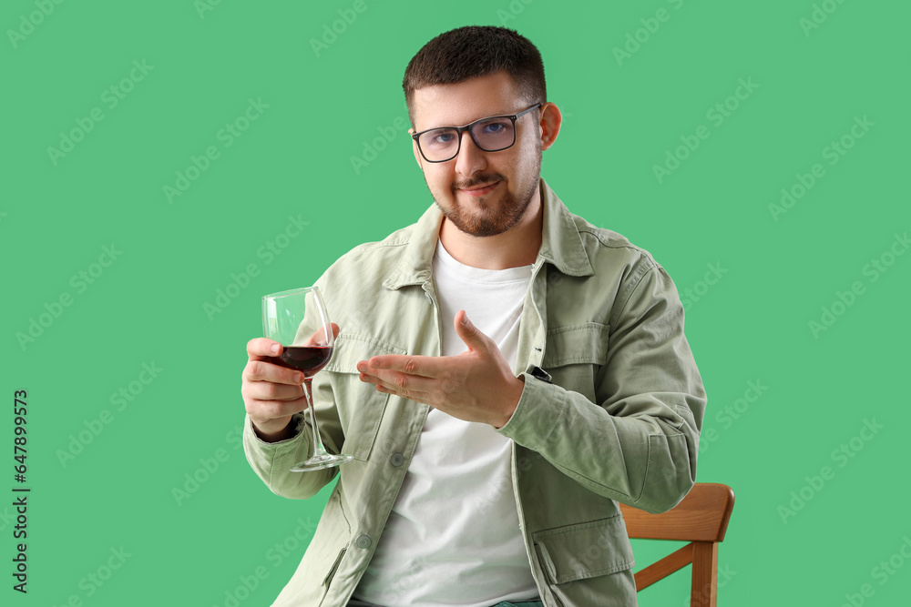 Young sommelier showing glass of wine on green background
