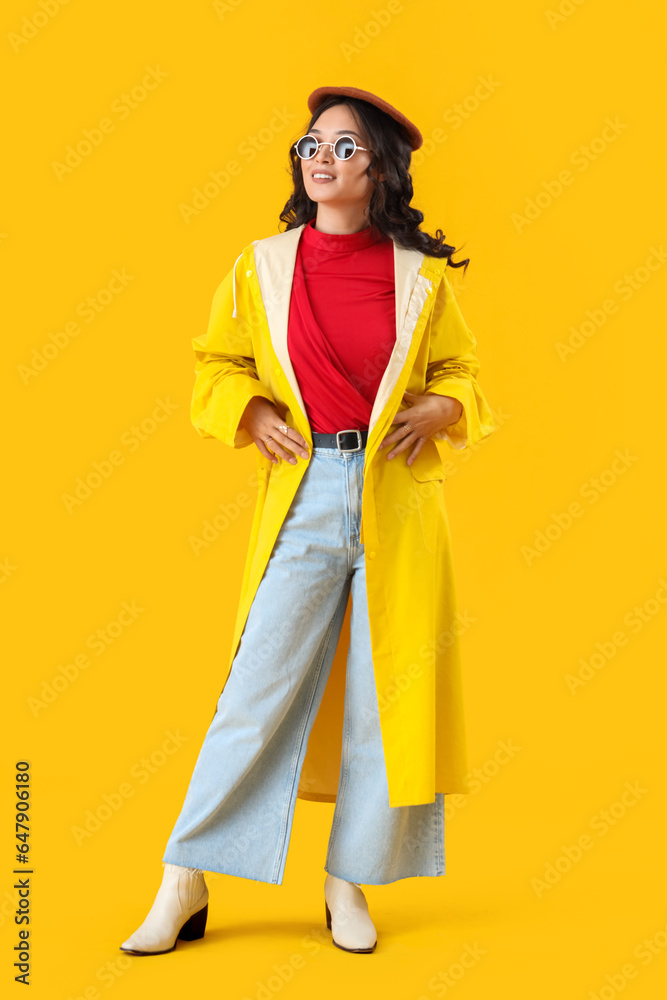Stylish young Asian woman in fall clothes on yellow background