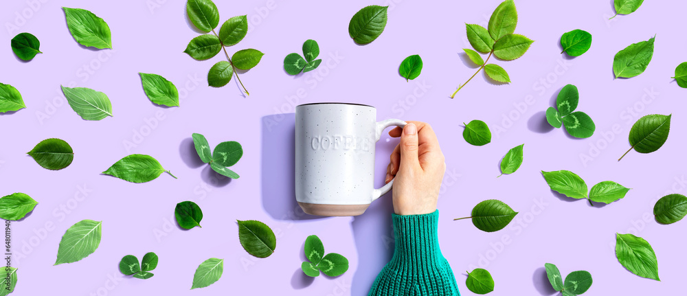 Person holding a mug with green leaves - flat lay
