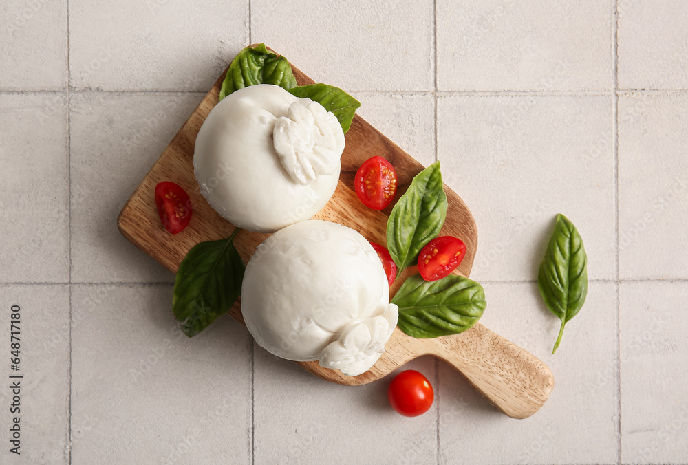 Wooden board of tasty Burrata cheese with basil and tomatoes on white tile table