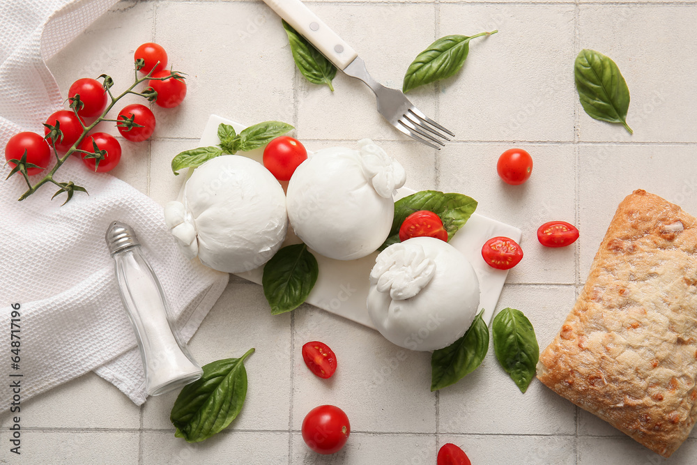 Board of tasty Burrata cheese with basil and tomatoes on white tile background
