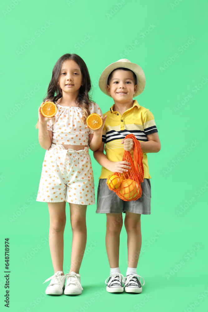 Little Asian children holding string bag with oranges on green background