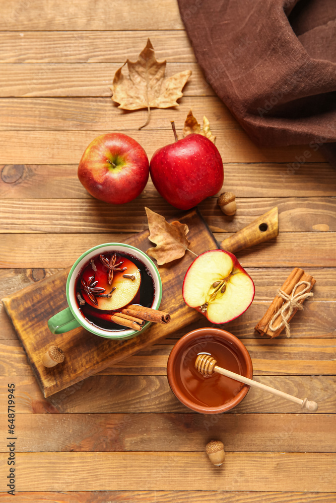 Cup of hot mulled wine with apple and bowl of honey on wooden background