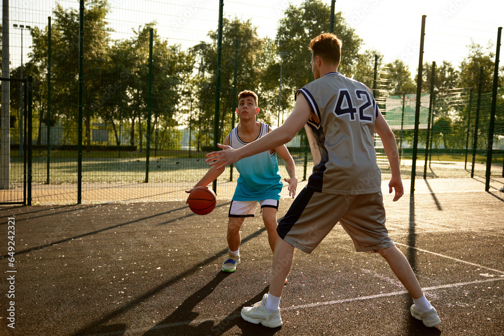 Active fit father and teenager son playing basketball on street court