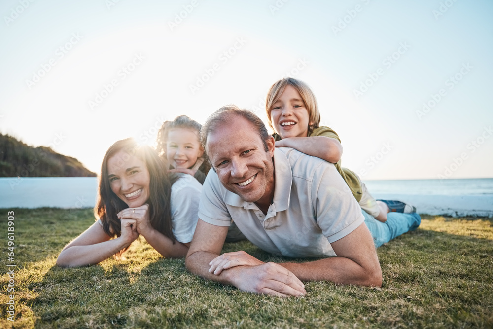 Family, parents and portrait of children on grass by ocean for bonding, relationship and relax together. Nature, sunlight and happy mother, father and kids on holiday, vacation and travel by sea