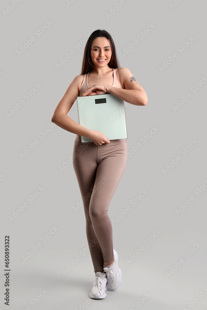Sporty young woman with scales on grey background
