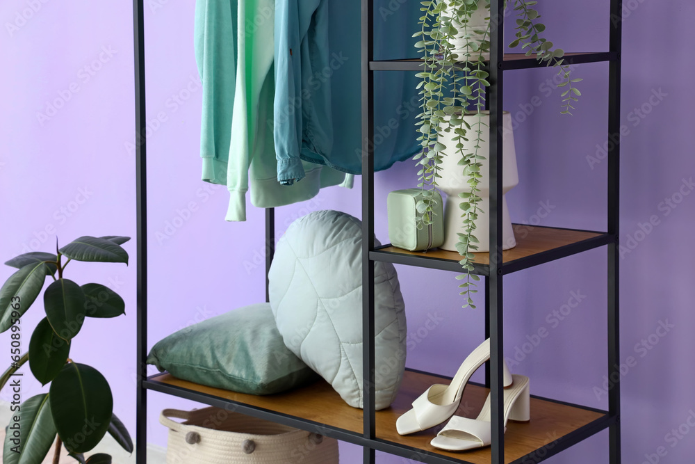 Shelving unit with pillows, shoes and houseplant near lilac wall