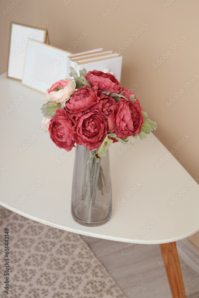 Vase with beautiful peony flowers on white table near beige wall, closeup