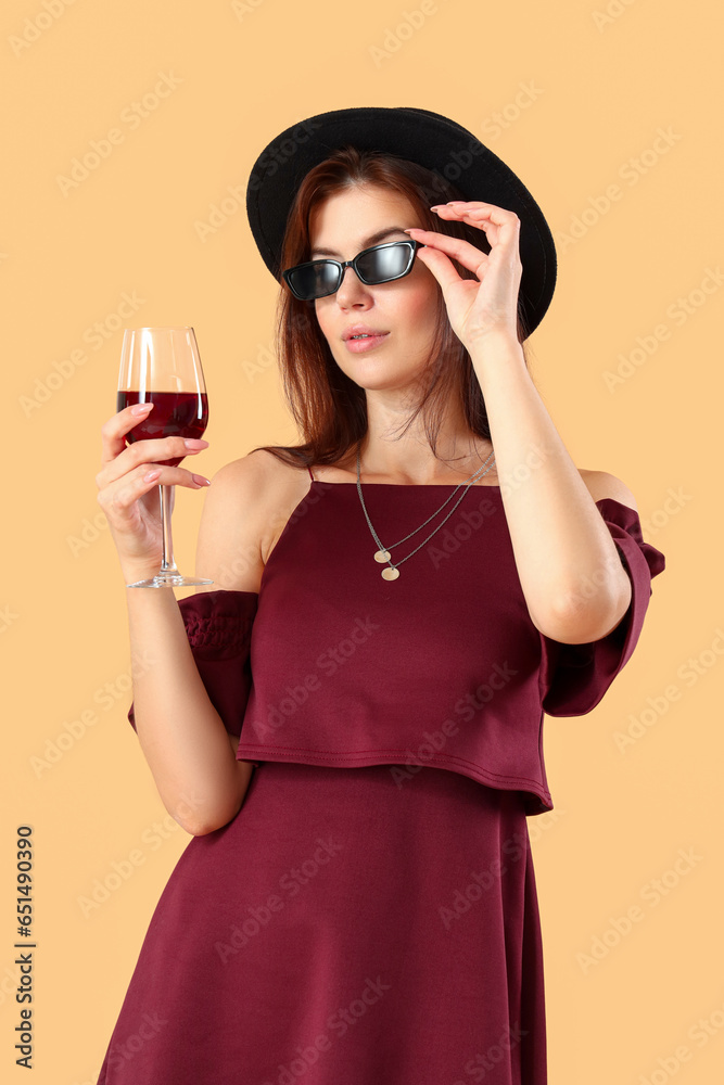 Beautiful young woman with glass of red wine on beige background
