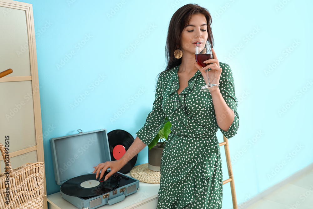 Beautiful young woman with glass of wine and record player at home