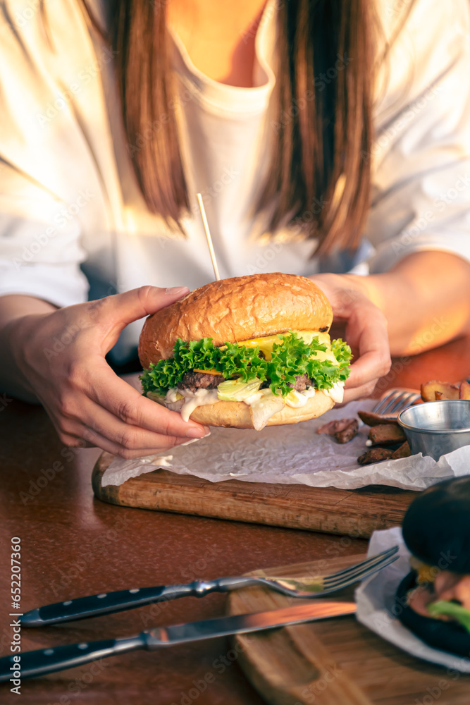 A young girl holding in female hands fast food burger, close up.