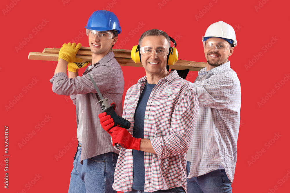 Team of male builders with wooden planks on red background