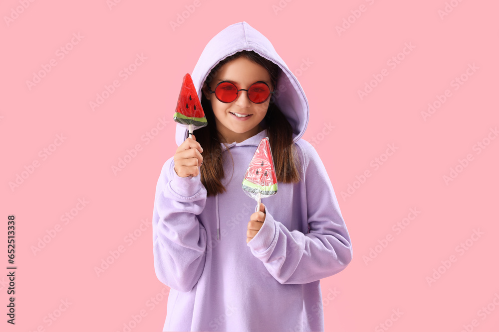 Happy little girl with lollipops in shape of watermelon slices on pink background