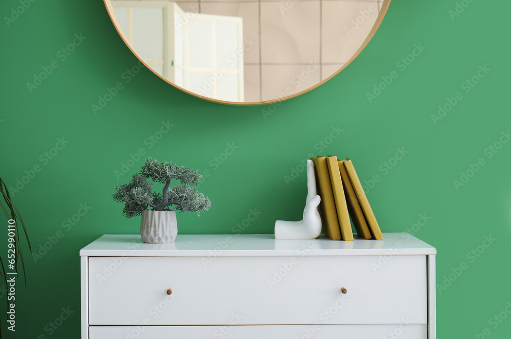 Stylish holder for books with bonsai on commode near green wall