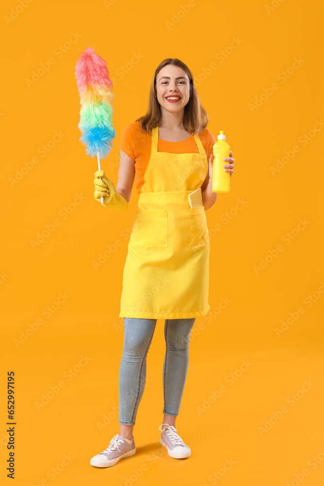 Young woman with bottle of detergent and pp-duster on orange background
