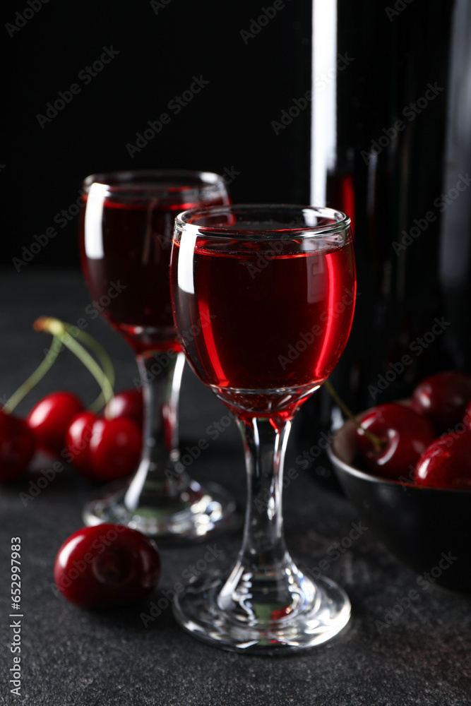 Glasses with sweet cherry liqueur on black background
