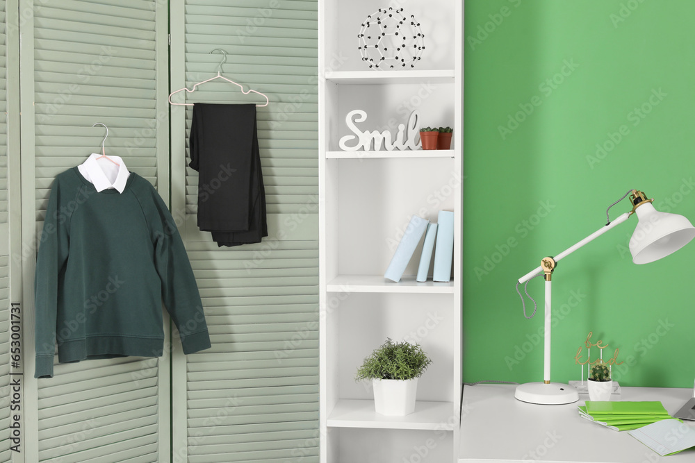 Shelving unit with decor, lamp stylish school uniform hanging on folding screen in room