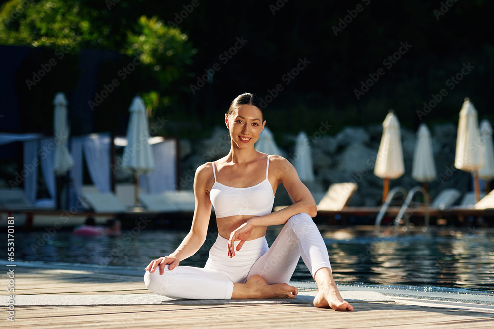 Woman near pool is doing yoga exercises
