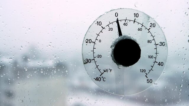 Raindrops and sleet on a thermometer outside the window that shows the air temperature outside. Weather forecast, thaw in winter beginning of spring. Copy space for text