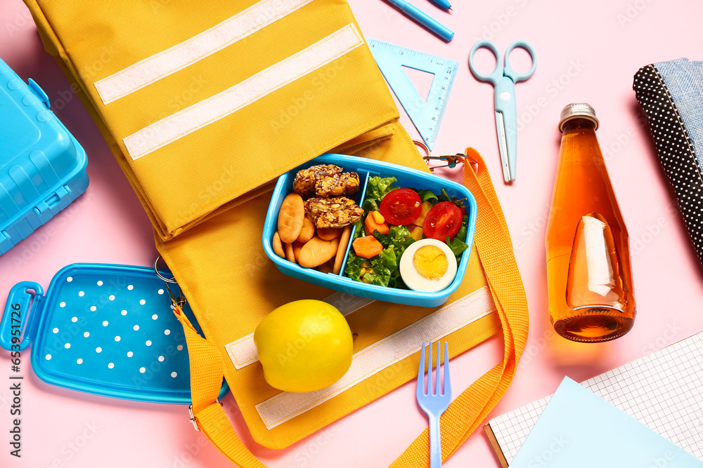 Backpack, stationery, bottle of lemonade and lunchbox with tasty food on pink background