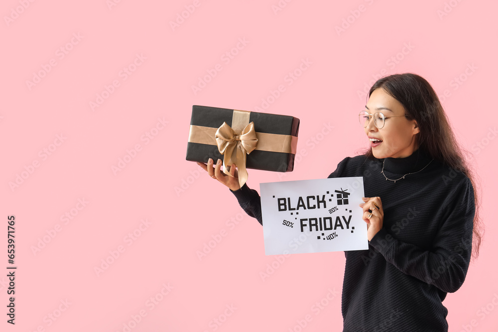 Surprised young Asian woman with gift on pink background. Black Friday sale