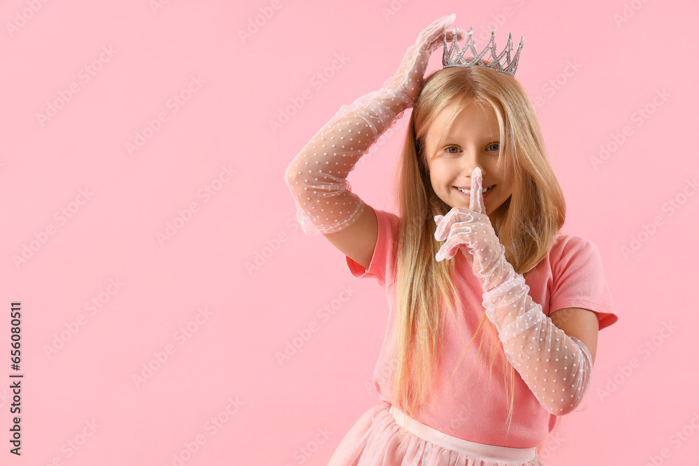 Cute little girl in tiara showing silence gesture on pink background