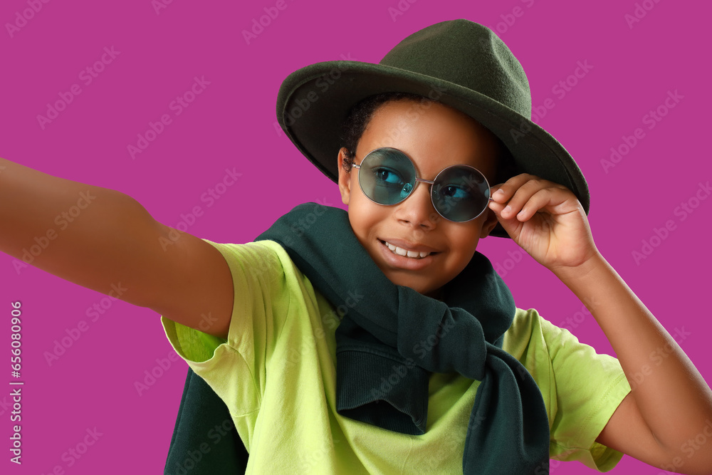 African-American little boy in hat and sunglasses taking selfie on purple background, closeup