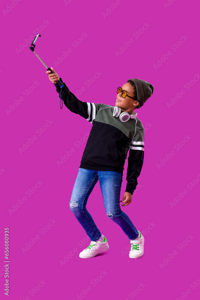 African-American little boy with mobile phone taking selfie on purple background